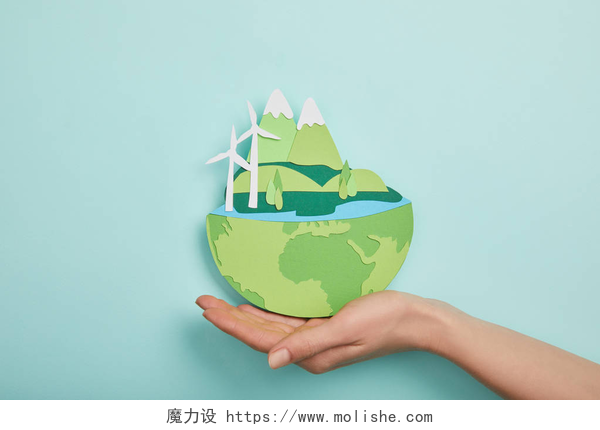 在蓝色背景下一双手托着一个环保地球的模型在绿松石背景下, 用可再生能源举行剪纸行星的顶级观点, 地球日概念